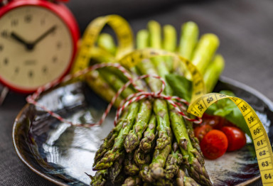 A tied bundle of asparagus next to a clock